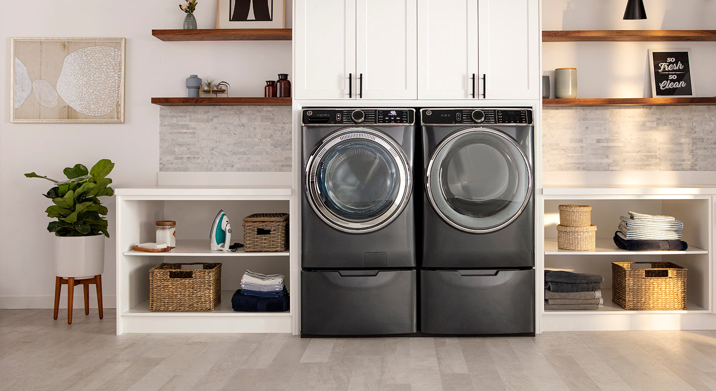 Modern laundry room with a front-load washer and dryer set against white, built-in cabinets and floating wood shelves.