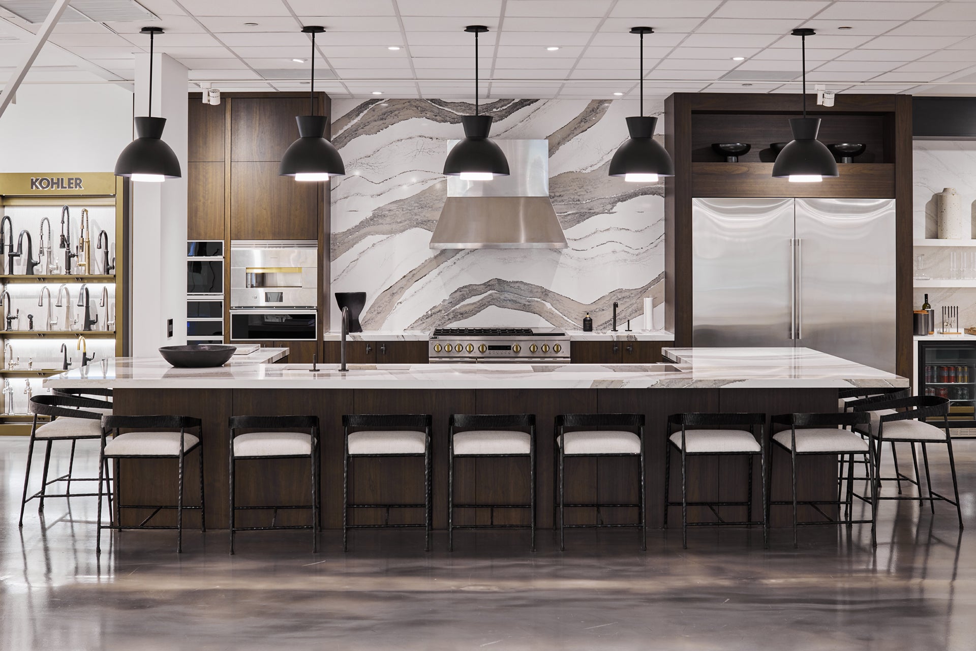 Modern kitchen showroom with stainless steel appliances by Monogram, dark wood cabinetry and marble countertops.