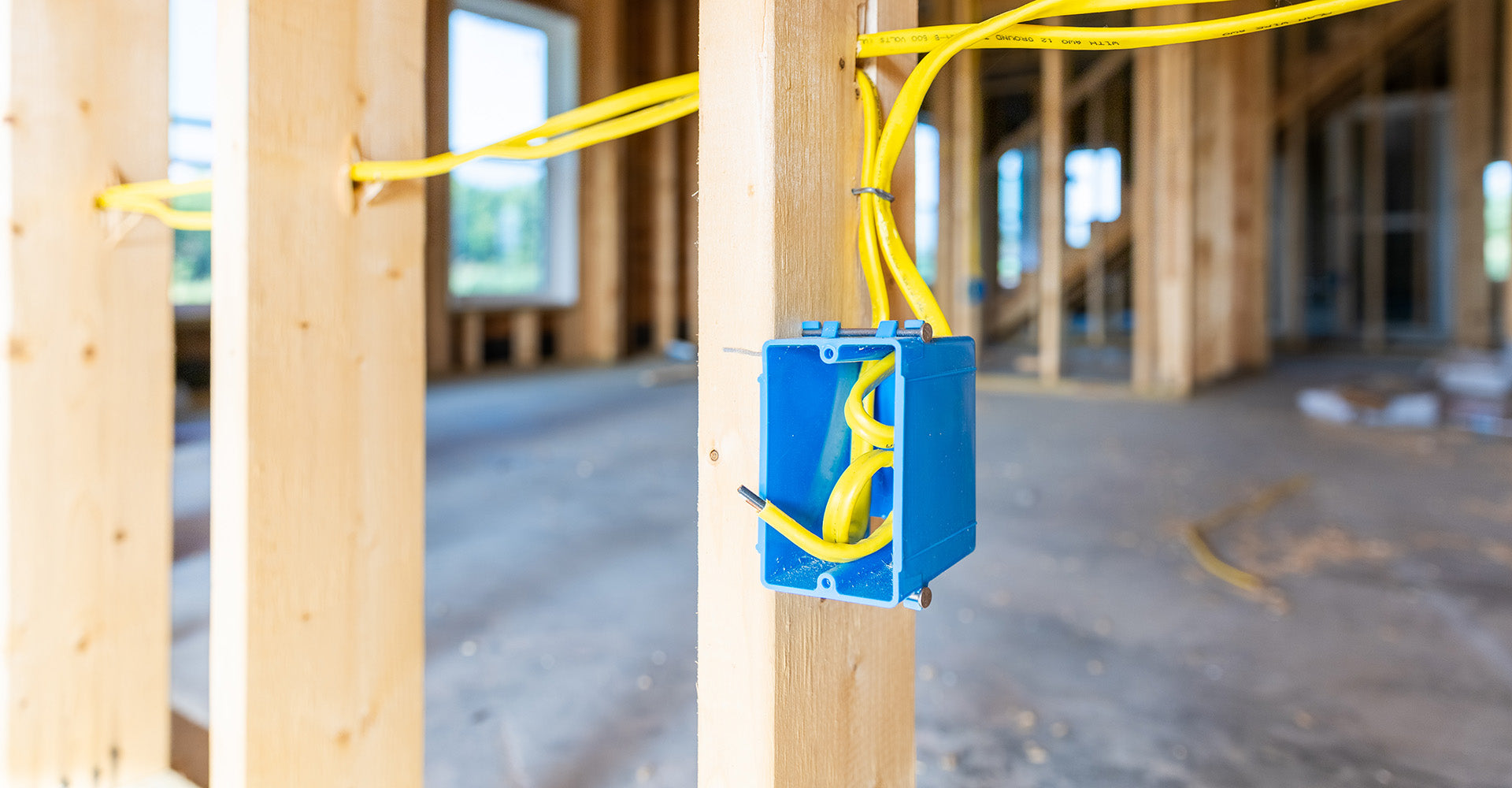 Blue plastic electrical box with yellow wires in a wooden framed room