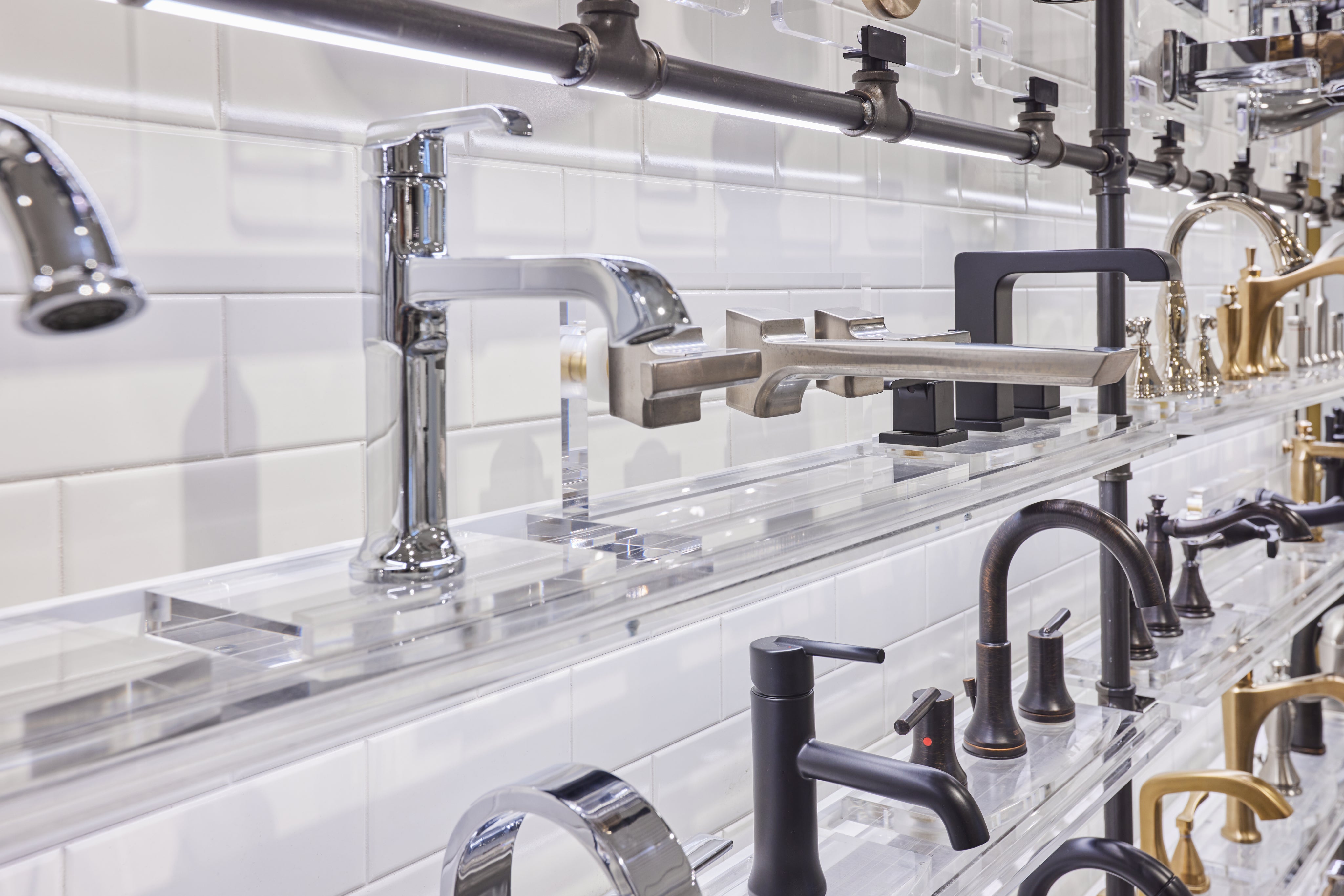 Display of various kitchen faucets and fixtures on a white tiled wall.