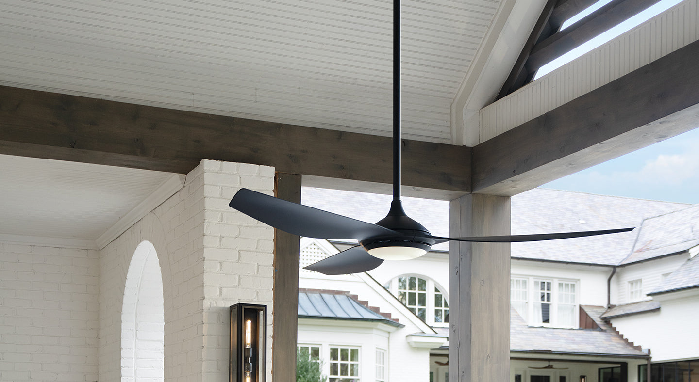 Ceiling fan hanging from a covered porch ceiling with a house in the background