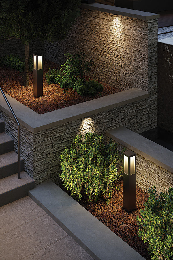 Outdoor lighting fixtures illuminating a stone wall and plants at night.