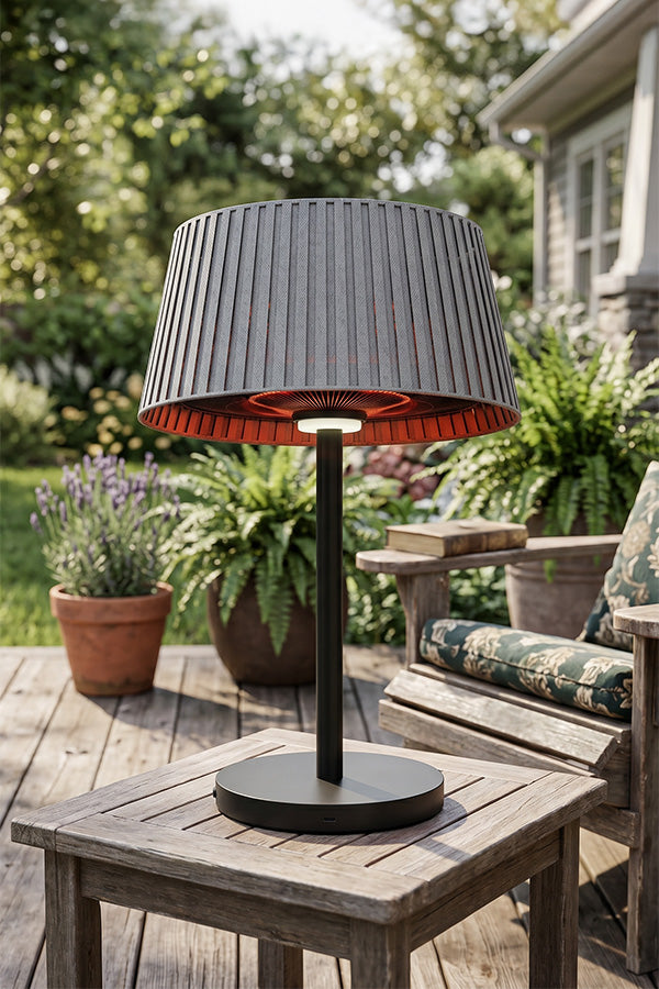 Outdoor table lamp that doubles as a heater with pleated shade on a wooden table in a garden setting