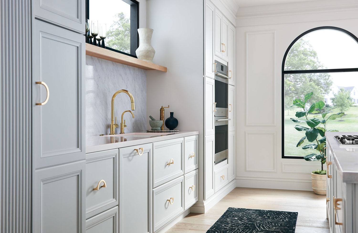 Modern kitchen with light gray cabinets, gold fixtures, and a large window.