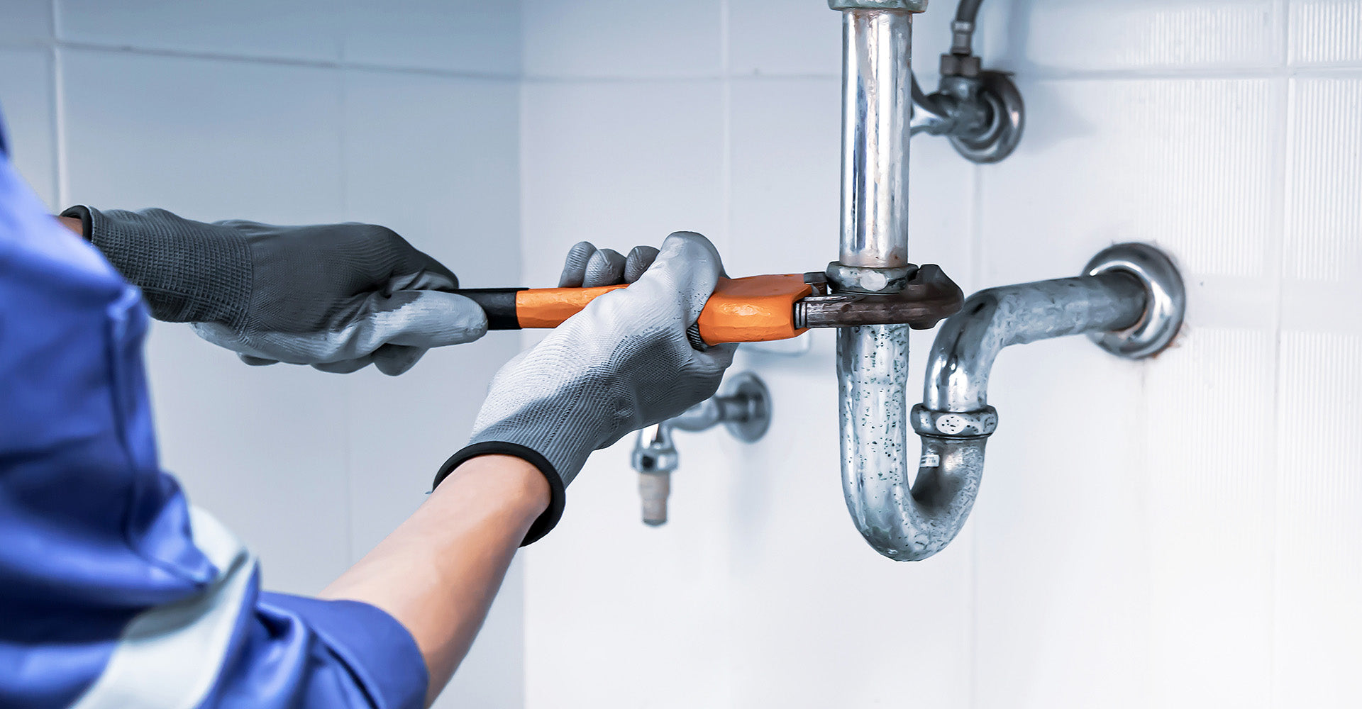 Person fixing a pipe with a wrench in a bathroom setting
