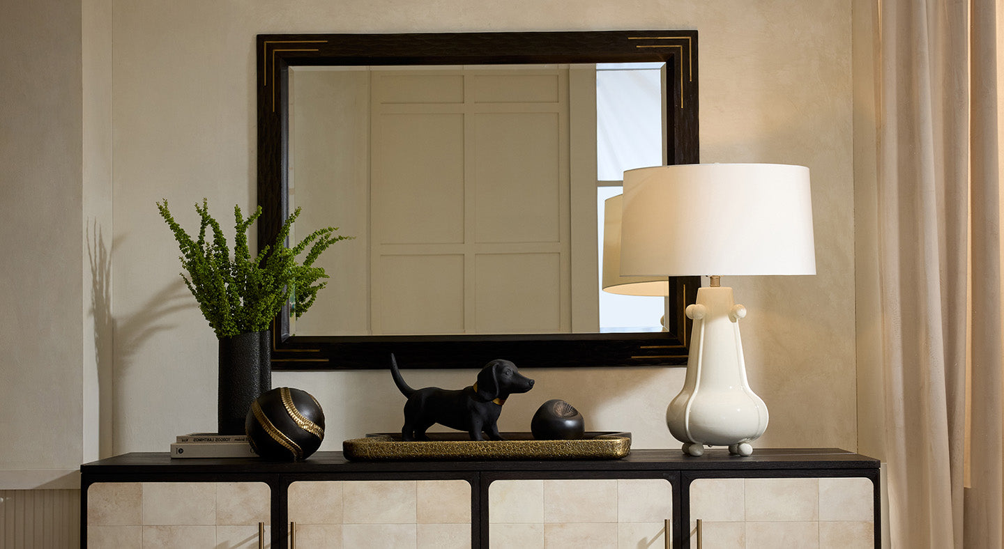 Decorative console table with a mirror, white lamp, and small dog figurine in a room.