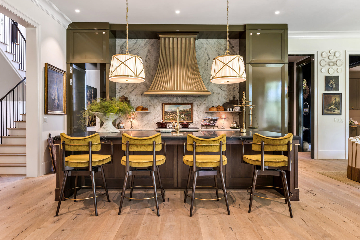 Modern kitchen with a custom range hood, two large pendant lights, yellow chairs and light wood flooring