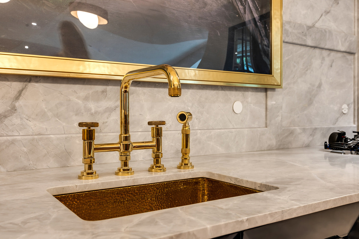 Gold faucet and hammered bar sink in with marble walls and countertop.