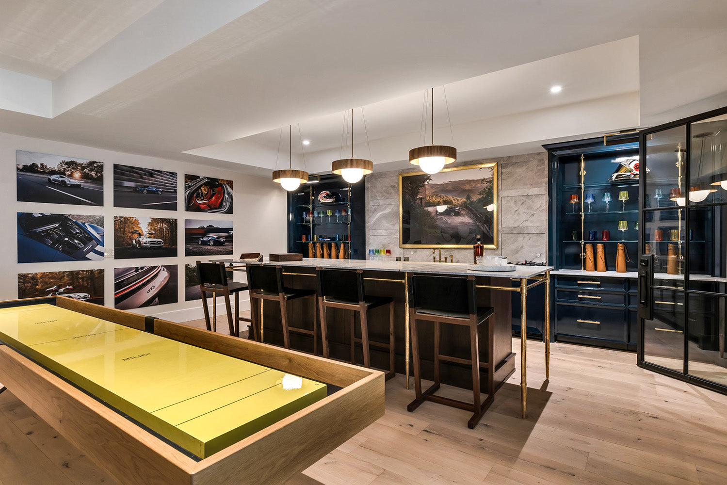 High end finished basement with a full bar, island with three pendant lights overhead, and a shuffleboard table