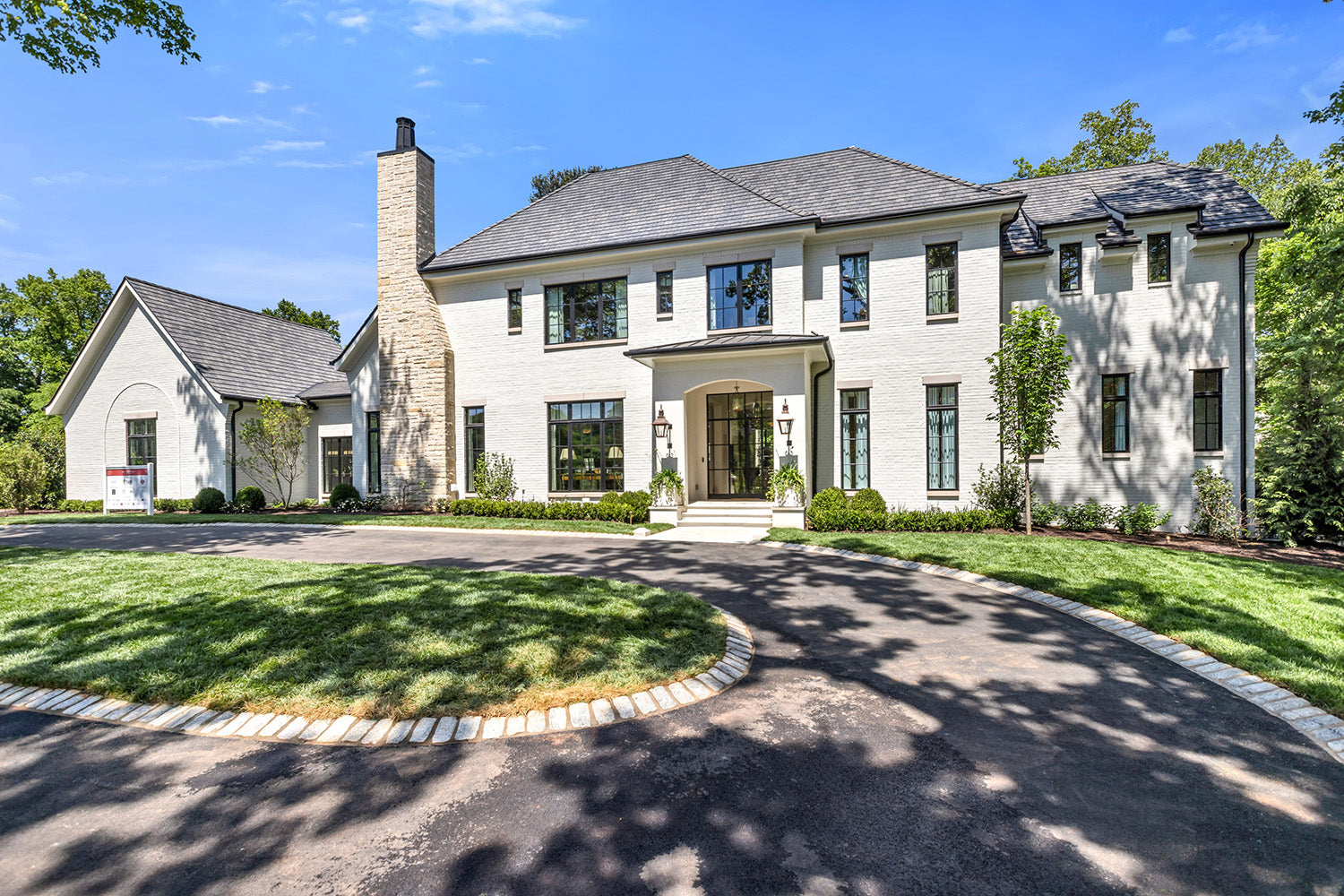Exterior of the 2026 Southeastern Designer Showhouse in Atlanta. Large white house with a driveway and green lawn under a blue sky.