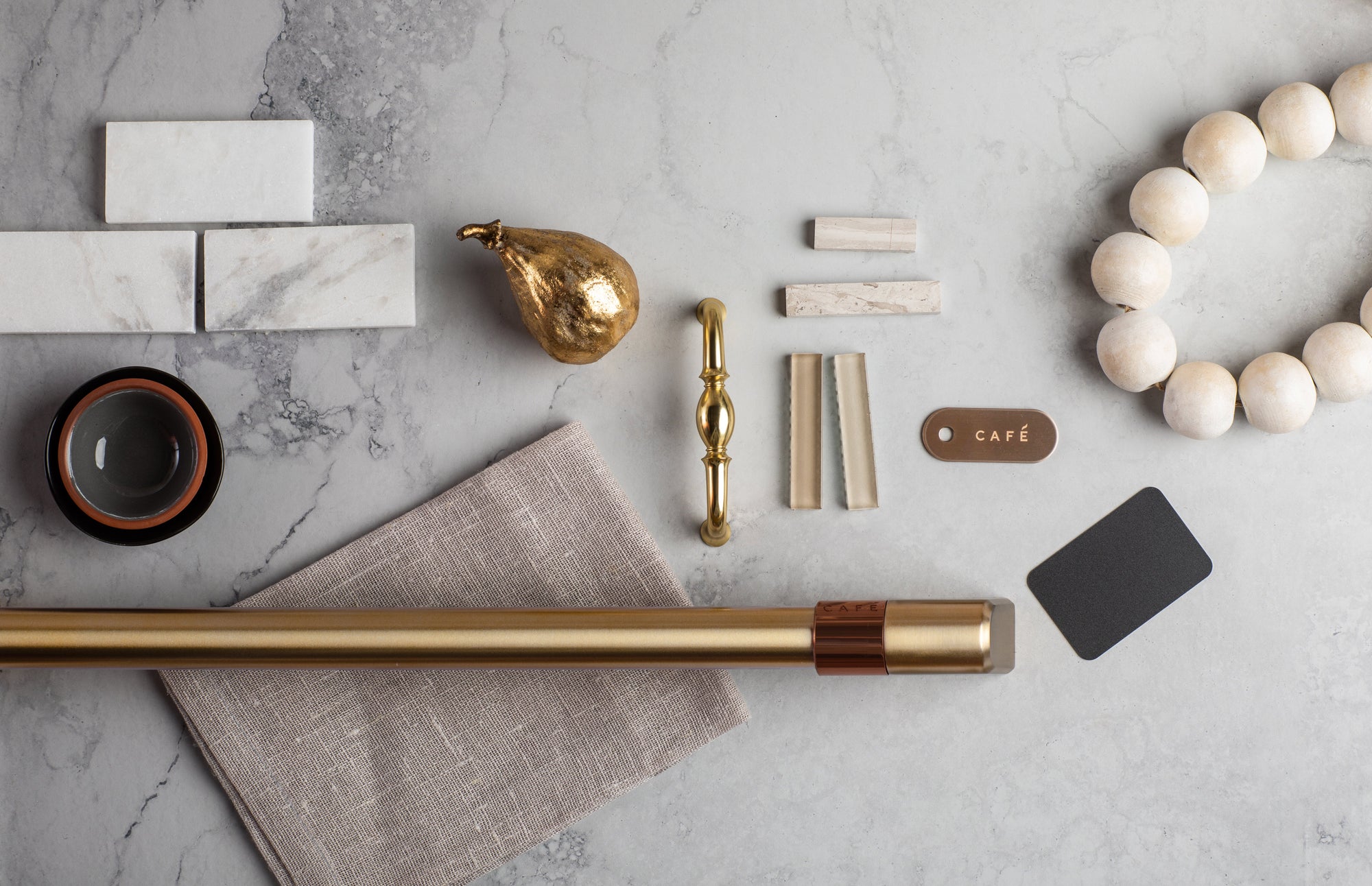 Collection of decorative items including a gold candle holder, marble tiles, and a wooden wreath on a gray surface.